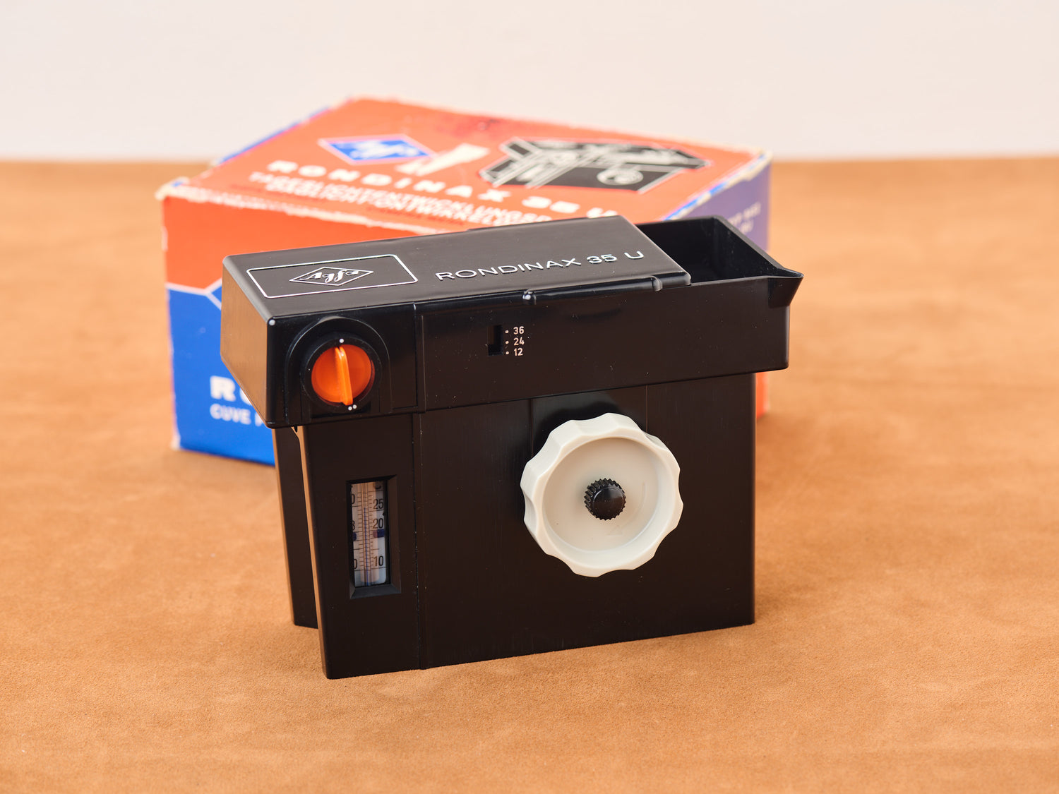 Agfa Rondinax 35U film tank on tan surface.Sleek, knobbed, dial-set, and ready to develop secrets in the dark.