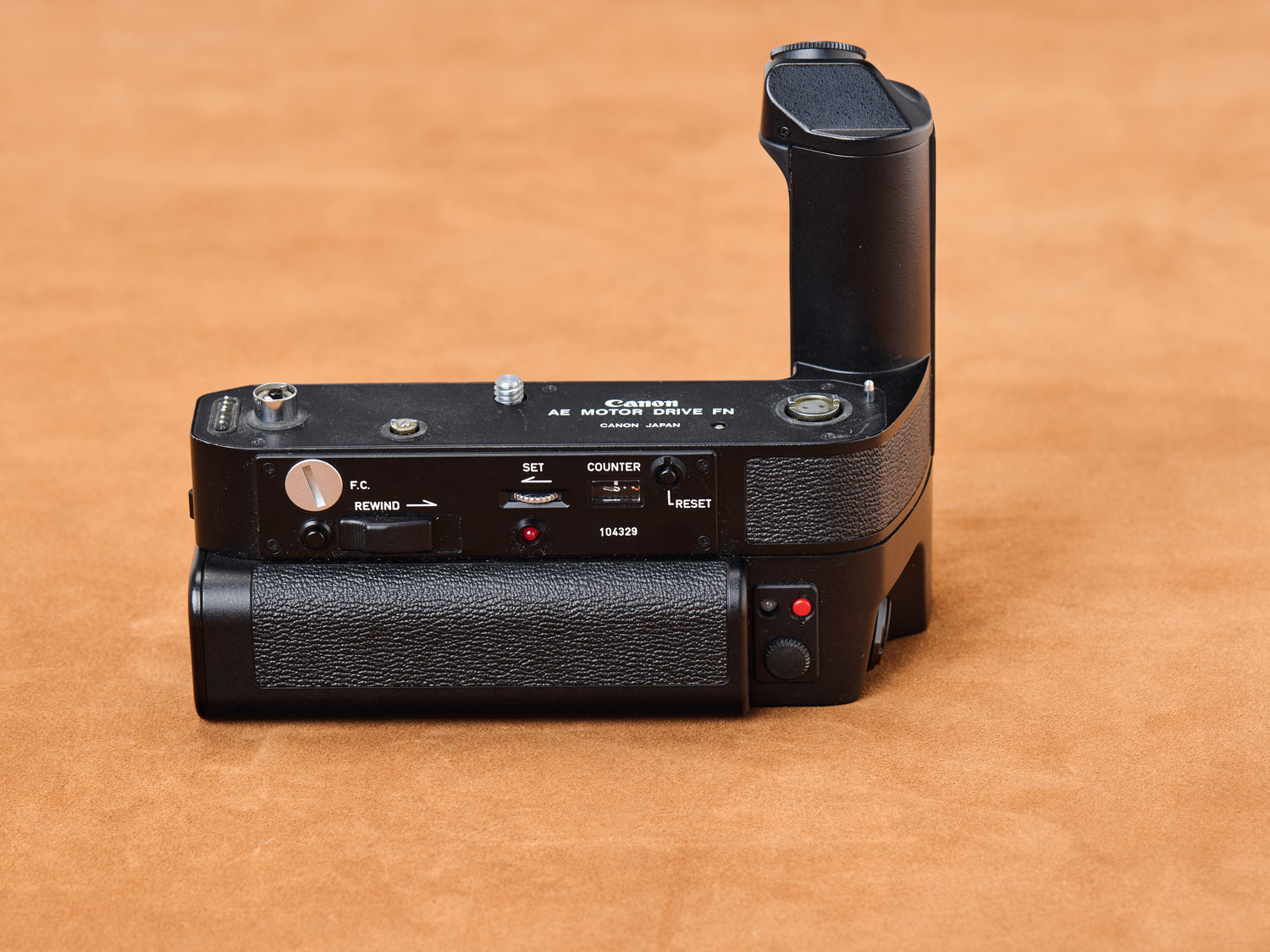 Canon new F-1 Motor Drive on suede, black body breathing heat. Rewind whirrs, counter ticks, red lights wink. Vertical grip rises, taut. Shhh. Come closer now.