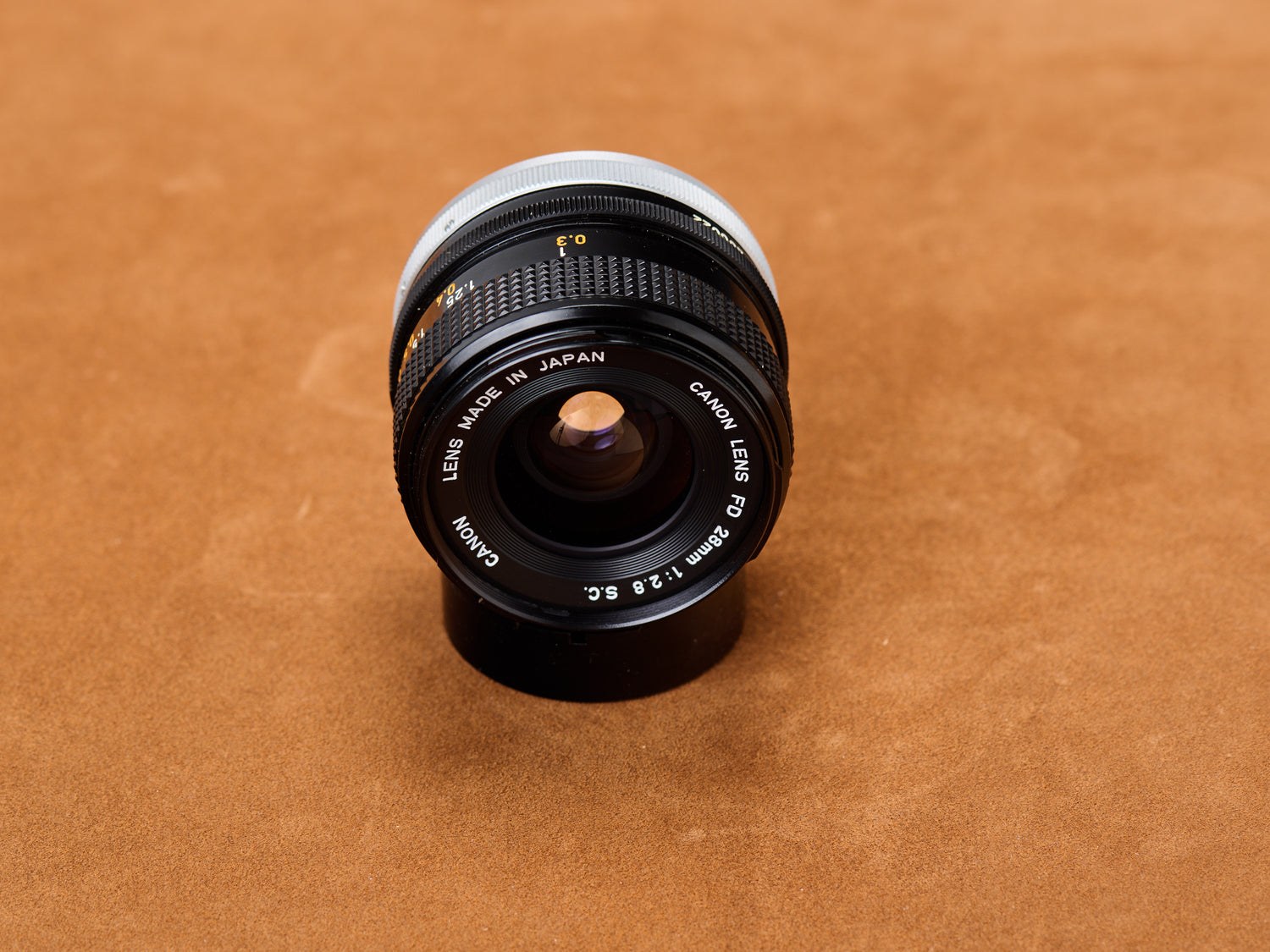 Canon 28mm f/2.8 FD S.C., black barrel trimmed in chrome. Front glass broods deep. Engraved specs sharp as a confession before the night goes quiet.