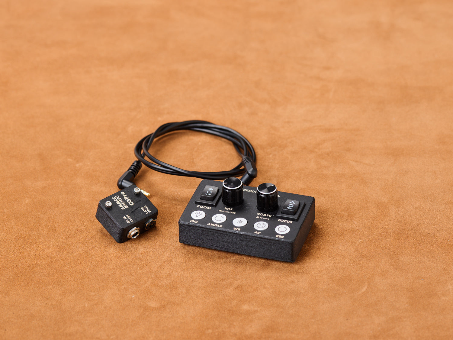 Cine Gear Pro BMMCC Remote Controller coiled, waiting. Black. Compact. Iris and Focus knobs beg for fingers. Coiled cable snakes to adapter. Twist. Control. Seduce.