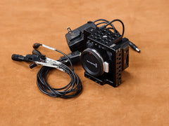 Blackmagic Micro Cinema Camera caged tight, cables coiled like secrets. Shadows hint at something just out of reach. 