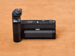 Canon Motor Drive FN sprawled on suede, black and dangerous. Vertical grip rises like a promise. Thumb finds the shutter. Motor coils, hungry. Tchk-tchk-tchk. Let go.