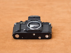 Canon new F-1 baseplate, obsidian underside glinting. Tiny scratches whisper secrets. Battery cover slides with sultry precision. Cold metal, intimate touch. Listen close.
