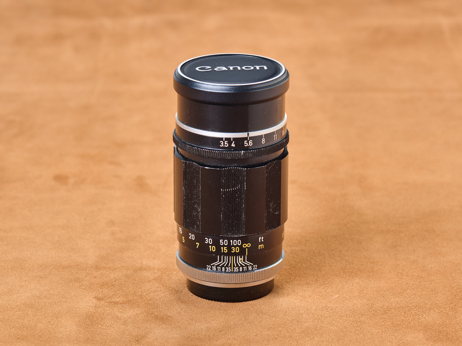 Vintage Canon 135mm f/3.5, black barrel set at f/5.6. Silver base glints. White numerals whisper secrets. Touch the focus ring. Come closer now.