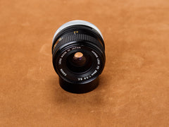 Canon 28mm f/2.8 FD S.C., black barrel trimmed in chrome. Front glass broods deep. Engraved specs sharp as a confession before the night goes quiet.