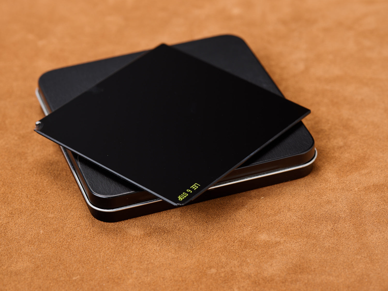 LEE Filters Little Stopper 100mm 6-stop ND 1.8 optical glass filter resting on black protective metal tin