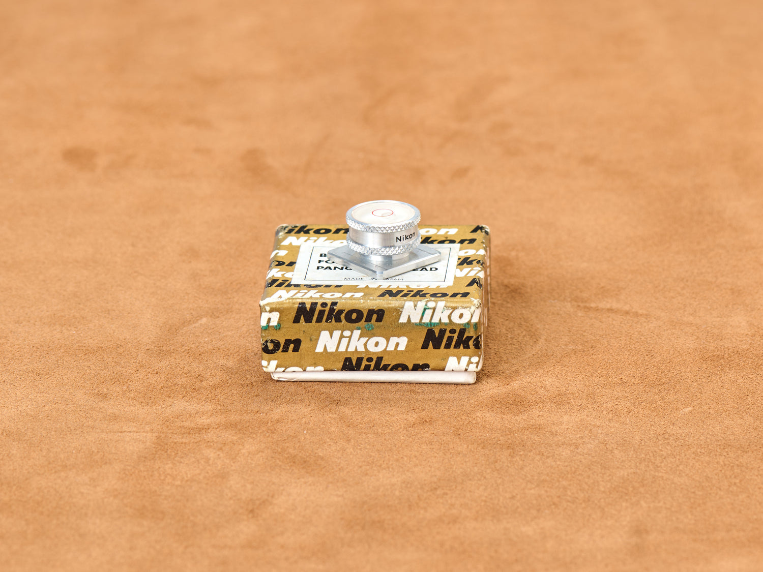 Vintage Nikon accessory shoe spirit bubble level in polished aluminum resting on original gold box